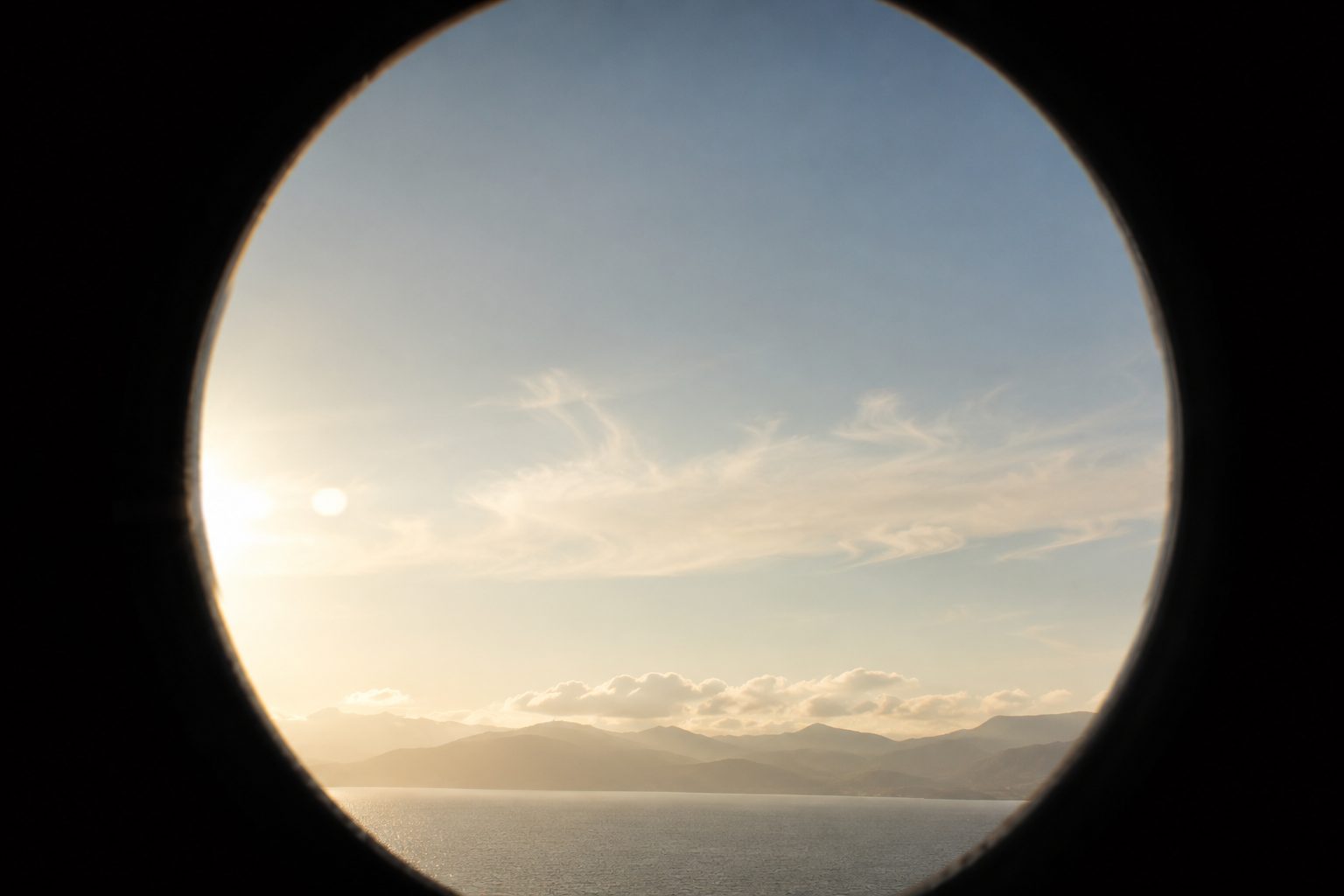 Ronde telescoopblik over zee richting de kust bij zonsondergang.